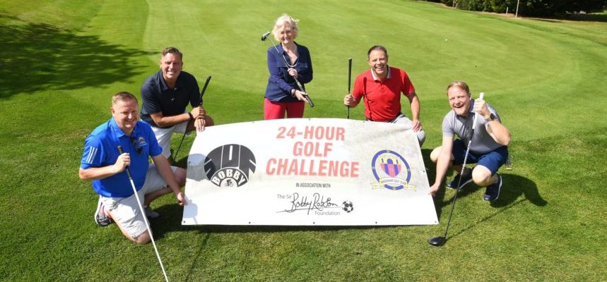 Lady Elsie and group holding 24 hour golf challenge poster on putting green.